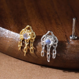 May include: Two stud earrings with flat back posts, one gold-toned and one silver-toned. Each features an ornate, cloud-like top set with a small, iridescent round stone and three delicate dangling chains hanging from the bottom edge.
