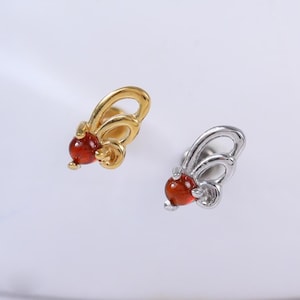 May include: Two butterfly-shaped earrings. One is gold-colored, the other is silver-colored. Both earrings feature a red gemstone at the center. The earrings are small and delicate, suitable for everyday wear. The background is white.