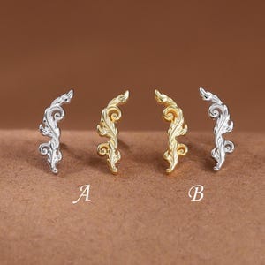 May include: Four curved stud earrings arranged in a row, featuring intricate scrollwork patterns. The two outer earrings are silver-toned, while the two inner earrings are gold-toned. The letters A and B are positioned below the pairs.