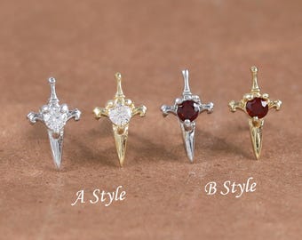 May include: Four small cross-shaped earrings. Two are silver-toned with clear stones, and two are gold-toned with red stones. The text "A Style" and "B Style" are below the earrings. The earrings are on a brown surface.