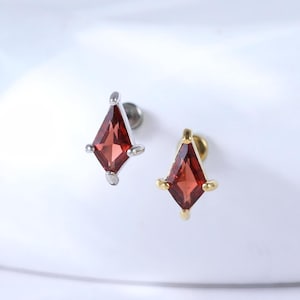 May include: Two stud earrings with a diamond-shaped, deep red gemstone. One earring has a silver-colored setting with small, silver accents. The other earring has a gold-colored setting with gold accents.