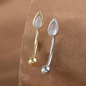 May include: A pair of earrings, one gold and one silver, each featuring a teardrop-shaped gemstone. The earrings have a long, slender design with a small ball at the base. The gemstones are a light, translucent color.