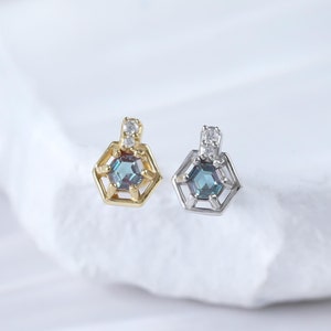 May include: Two geometric earrings with a blue gemstone in the center and a small clear stone at the top. The earring on the left is gold and the earring on the right is silver.