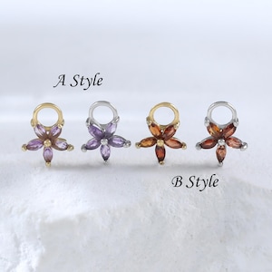May include: Four flower-shaped earrings with gemstone petals. Two pairs are labeled "A Style" and "B Style". The earrings have gold and silver accents. The gemstones are purple, orange, and red. The earrings are displayed on a white surface.