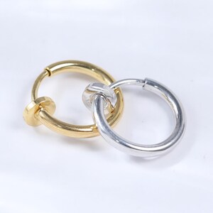 May include: A pair of hoop earrings, one gold-toned and one silver-toned, interlocked. The gold earring has a small, round clasp. The silver earring is a simple, smooth hoop. The earrings are displayed on a white surface.