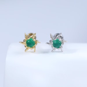 May include: Two stud earrings, one gold-toned and one silver-toned, each featuring a central green gemstone. The earrings have a starburst design around the gemstone. The earrings are displayed on a white surface.