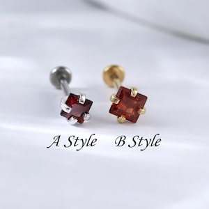 May include: Two styles of small, square red gemstone earrings. The earring on the left has a silver post and the earring on the right has a gold post. The earrings are labeled "A Style" and "B Style".