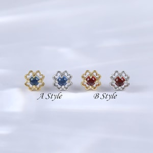 Puede incluir: Cuatro pequeños pendientes decorativos con un diseño en forma de flor. Los pendientes están disponibles en dos estilos: A y B. El estilo A presenta una piedra preciosa azul, mientras que el estilo B presenta una piedra preciosa roja.