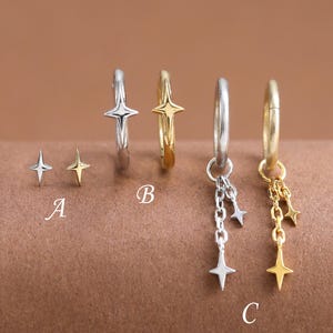 May include: A collection of star-shaped earrings in silver and gold. The earrings include stud earrings, hoop earrings with star accents, and hoop earrings with dangling star charms. The earrings are displayed on a brown surface.