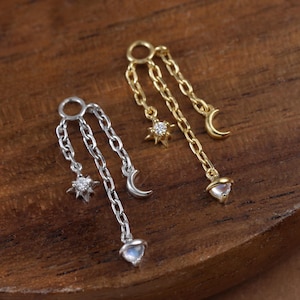May include: Two delicate earrings with celestial charms. One earring is silver-toned, featuring a star, crescent moon, and heart-shaped charm. The other is gold-toned, with a star, crescent moon, and a heart-shaped charm. Both earrings have a chain design.