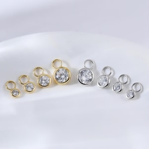 Może przedstawiać: Zestaw małych, okrągłych, przezroczystych zawieszek z kryształu z złotymi i srebrnymi kółkami. Zawieszki są ułożone w rzędzie na białym tle.