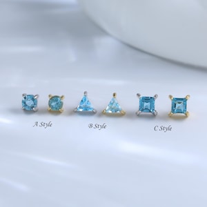 May include: A selection of small, light blue gemstone stud earrings in different shapes: round, triangular, and square. Each earring is set in a silver or gold-coloured metal. The image includes text labels: "A Style", "B Style", and "C Style".