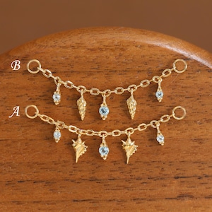 May include: Two gold-toned chain connectors labelled A and B, each featuring small dangling charms. Chain B has three shell-like charms and two light blue round stones. Chain A has two shell-like charms and three light blue round stones.