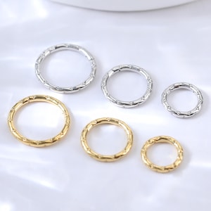 May include: Six assorted metal rings in gold and silver tones. The rings vary in size and feature a textured, bamboo-like design. The rings are arranged on a white surface, showcasing their different sizes and finishes. Ideal for jewelry making or crafting.