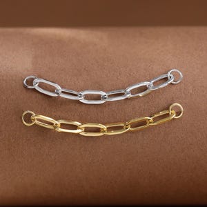 Könnte beinhalten: Zwei kurze Schmuckkettensegmente, eines in poliertem Silberton und eines in poliertem Goldton. Jedes Segment besteht aus fünf länglichen ovalen Gliedern mit einem kleinen runden Biegering an beiden Enden für eine sichere Verbindung.
