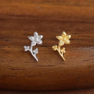 May include: Two small stud earrings shaped like delicate flower sprigs. One earring is finished in a bright silver tone, while the other is finished in a warm gold tone. Each piece features a five-petaled blossom at the top and small buds.