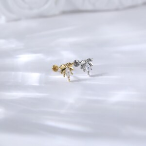 Puede incluir: Dos delicados pendientes de oreja, uno dorado y otro plateado, cada uno con un dise&ntilde;o en forma de hoja con una gema transparente en forma de l&aacute;grima. Los pendientes se presentan sobre un fondo blanco suave, resaltando sus detalles.