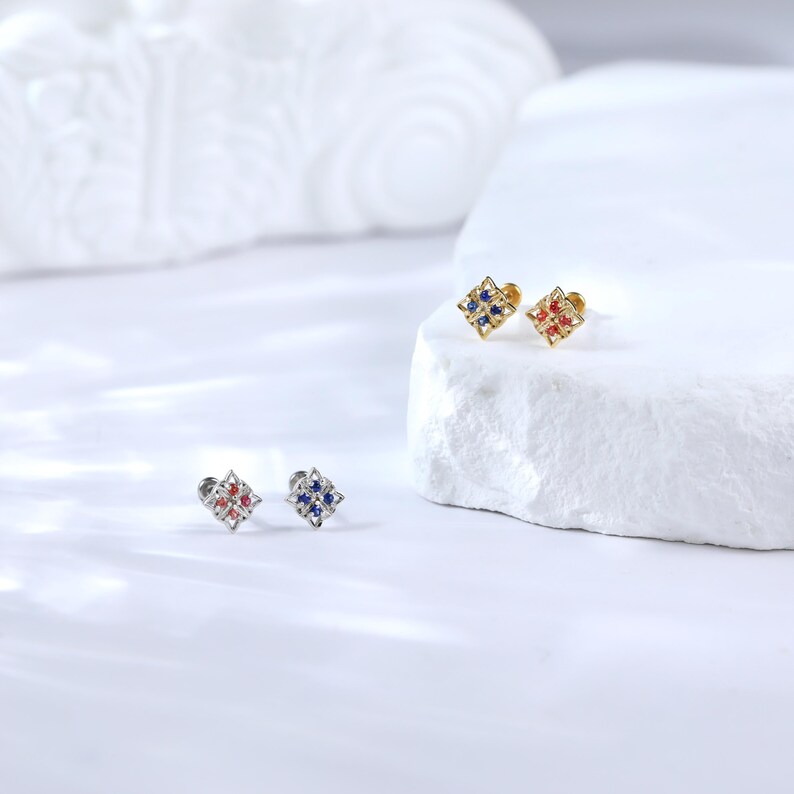 May include: Three pairs of small, square-shaped earrings with a decorative design. The earrings are available in gold, silver, and rose gold with blue and red gemstones.