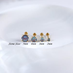 May include: Four gold body jewellery studs with different sized iridescent blue gemstones. The stones are 5mm, 4mm, 3mm, and 2mm in diameter. The text "Stone Size" is written below the studs.