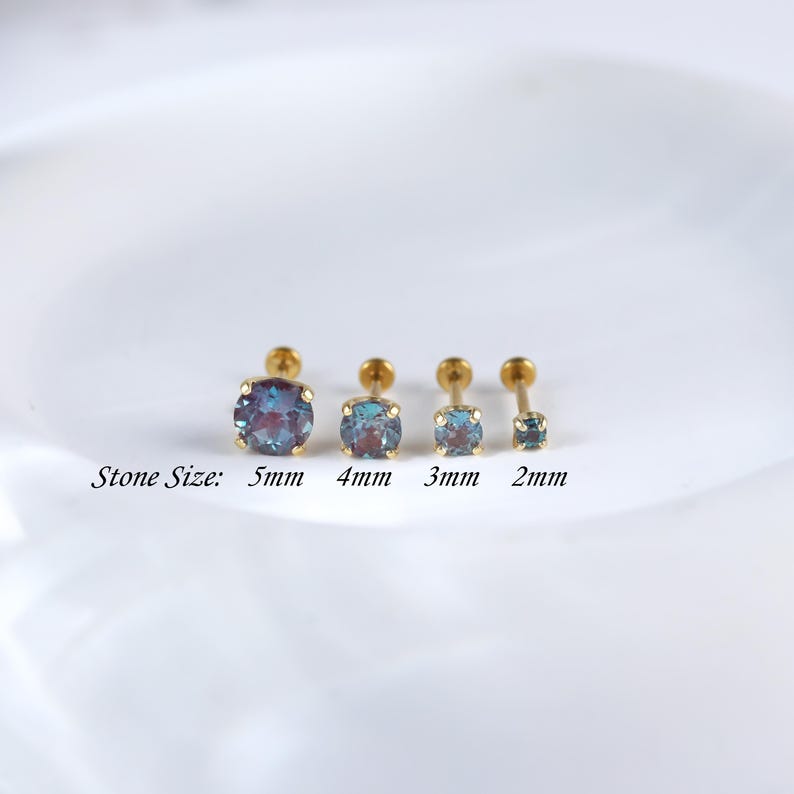 May include: Four gold body jewellery studs with different sized iridescent blue gemstones. The stones are 5mm, 4mm, 3mm, and 2mm in diameter. The text "Stone Size" is written below the studs.