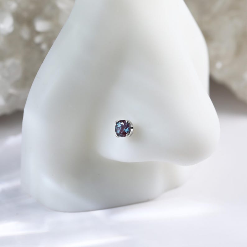 May include: A silver nose stud with a round, iridescent blue gemstone.