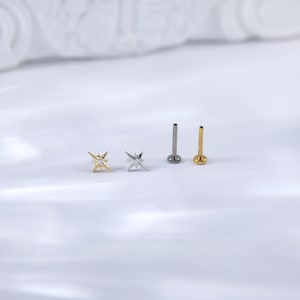 May include: Three silver and gold star-shaped body jewellery pieces with a clear gem in the centre. Two of the pieces are star-shaped and the third is a straight post.