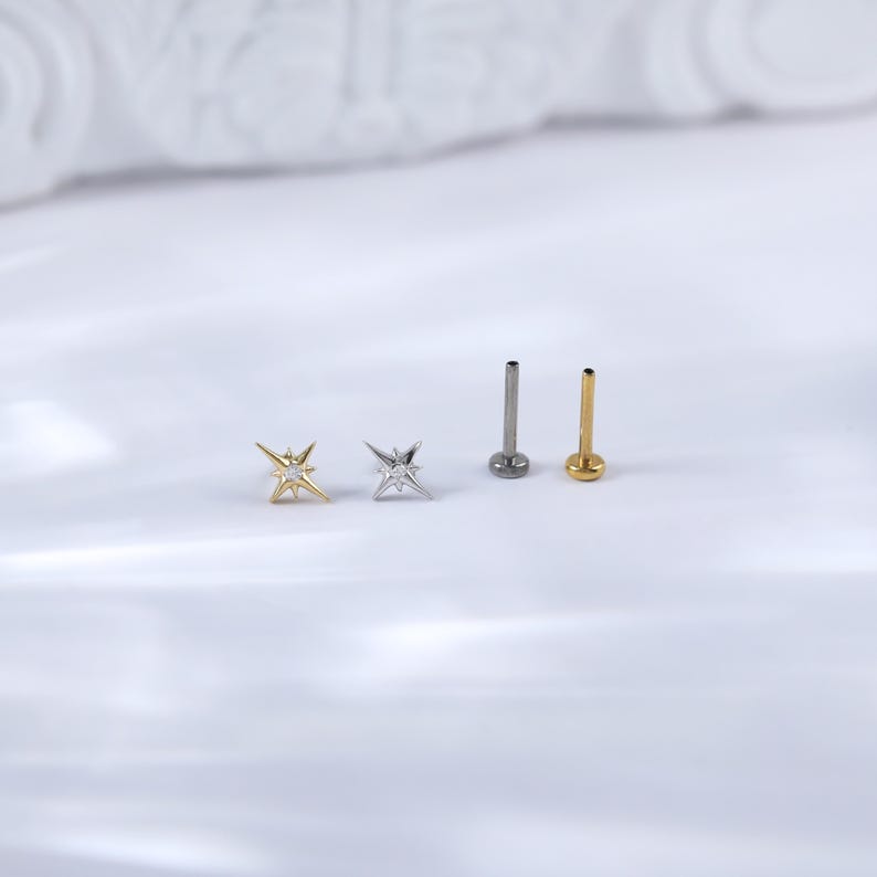 May include: Three silver and gold star-shaped body jewellery pieces with a clear gem in the centre. Two of the pieces are star-shaped and the third is a straight post.