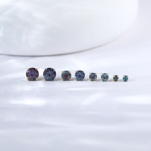 May include: A set of seven round gemstone earrings in various sizes. The earrings are set in silver and gold settings. The gemstones are a mix of blue, green, and purple.
