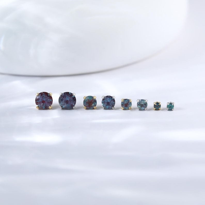 May include: A set of seven round gemstone earrings in various sizes. The earrings are set in silver and gold settings. The gemstones are a mix of blue, green, and purple.