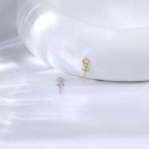 May include: Two small pendant charms. One is silver-colored, shaped like a rose with a cross. The other is gold-colored, shaped like a sword with a loop at the top. Both charms have small, clear accent stones.