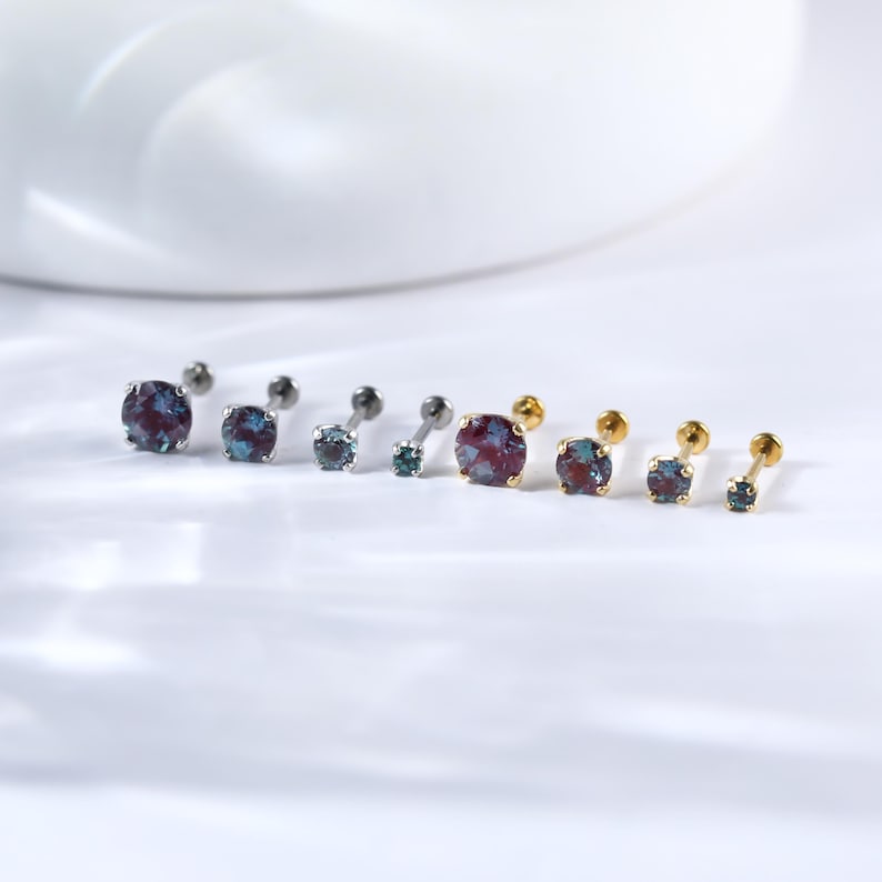 May include: A set of six body jewellery pieces with different coloured gemstones. The jewellery is made of surgical steel and gold. The gemstones are blue, green, and purple.