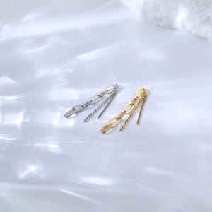May include: Two pairs of chain earrings. One pair is silver-toned, featuring a chain link design with a dangling beaded strand. The other pair is gold-toned, with a similar chain link design and a dangling beaded strand. The earrings are displayed on a white surface.
