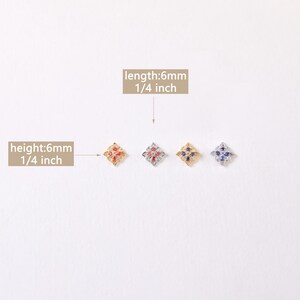 May include: Four small, square-shaped charms with a floral design. The charms are 1/4 inch in length and height. The charms are gold, silver, and have red and blue gemstones.