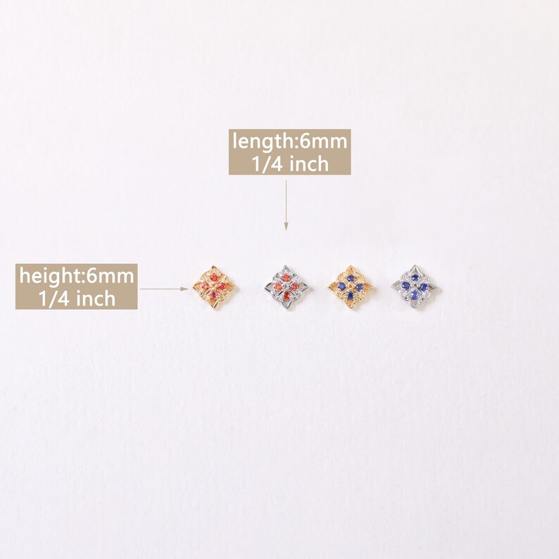 May include: Four small, square-shaped charms with a floral design. The charms are 1/4 inch in length and height. The charms are gold, silver, and have red and blue gemstones.