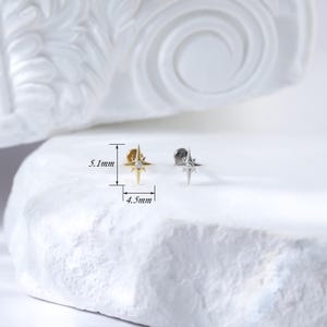 May include: Two gold and silver star-shaped earrings with a small clear stone in the centre. The earrings are 5.1 mm tall and 4.5 mm wide.