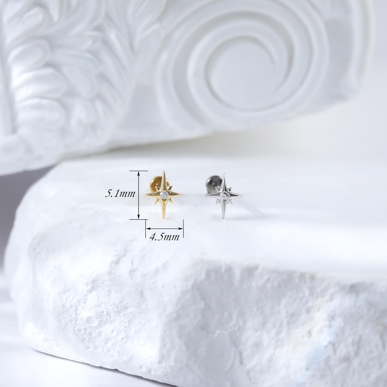 May include: Two gold and silver star-shaped earrings with a small clear stone in the centre. The earrings are 5.1 mm tall and 4.5 mm wide.
