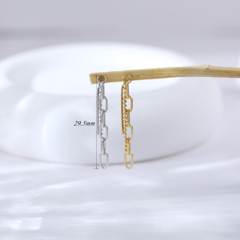 May include: Two chain earrings, one silver and one gold, are displayed against a soft, neutral background. The silver earring features a delicate, layered design, while the gold earring has a thicker chain. The earrings are approximately 29.5mm in length.