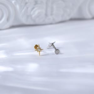 May include: Two star-shaped body jewellery pieces with a clear stone in the centre. One is gold and the other is silver.