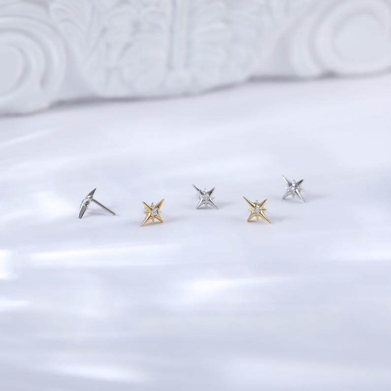 May include: Four small star-shaped earrings with a single clear stone in the centre. Two earrings are gold, and two are silver.