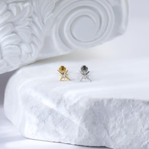 May include: Two star-shaped earrings with a small clear stone in the centre. The earring on the left is gold and the earring on the right is silver.