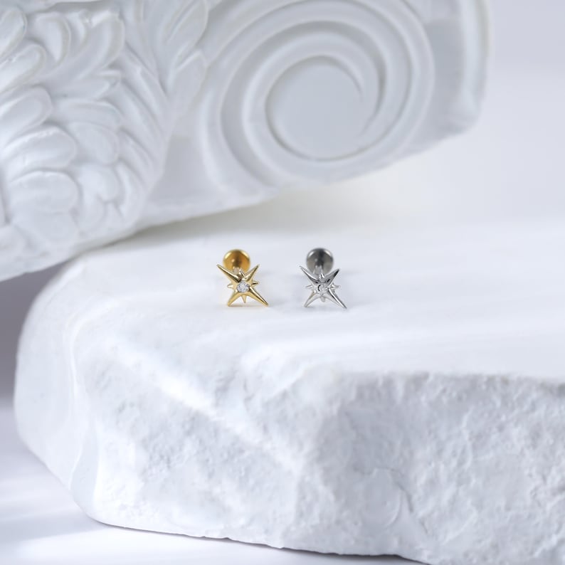 May include: Two star-shaped earrings with a small clear stone in the centre. The earring on the left is gold and the earring on the right is silver.