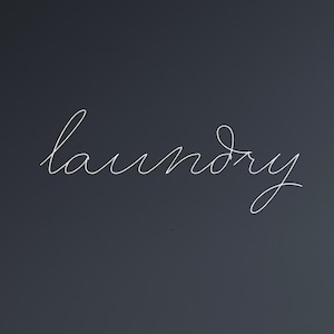 May include: A dark gray wall with the word "laundry" written in elegant white script. The wall is above a light-colored wooden floor. The image is a simple, clean design.