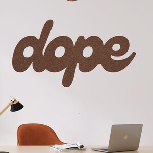May include: A home office setup featuring a light wood desk with black legs, a laptop, and a modern desk lamp. The word "dope" is displayed on the white wall. An orange chair and potted plants complete the scene, creating a stylish workspace.