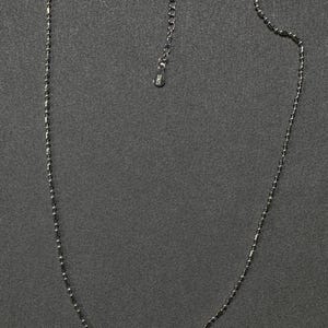 May include: A delicate silver necklace with a beaded design. The necklace features small, cylindrical beads strung together to form a chain. The clasp and extender chain are visible, and the necklace is displayed against a dark gray background.