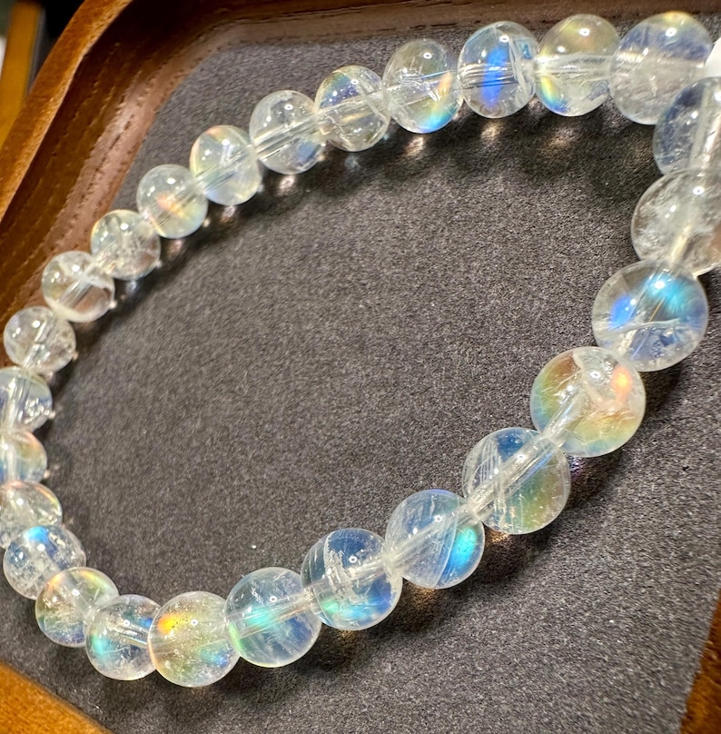 Pode incluir: Uma pulseira de contas transparentes e iridescentes. As contas redondas t&ecirc;m um brilho de arco-&iacute;ris, refletindo cores como azul, amarelo e verde. A pulseira &eacute; enfiada em um cord&atilde;o el&aacute;stico transparente.