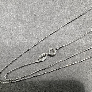 May include: A delicate silver necklace with a ball chain design. The necklace features a small clasp and a tag that reads "ITALY 925". The chain is displayed on a gray surface.
