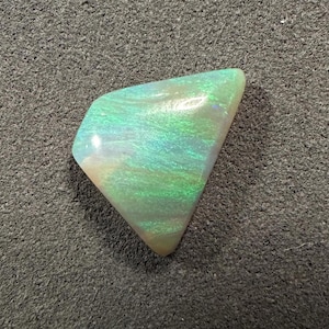 Può includere: Una pietra preziosa di opale verde e bianca di forma triangolare.