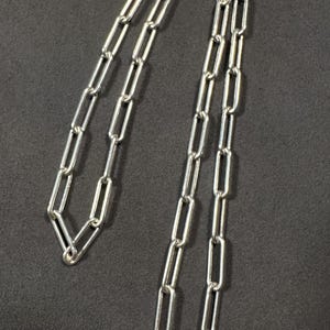 May include: A silver chain necklace with a lobster clasp fastening. The chain is made of small, rectangular links.