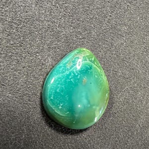 May include: A teardrop-shaped green and blue gemstone cabochon with a smooth, polished surface.