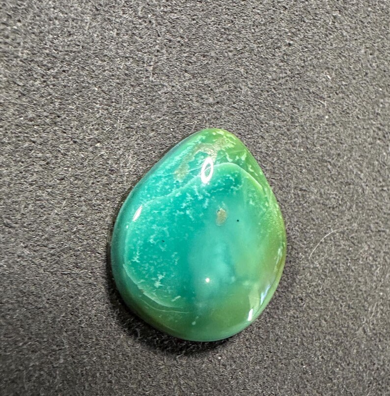 May include: A teardrop-shaped green and blue gemstone cabochon with a smooth, polished surface.